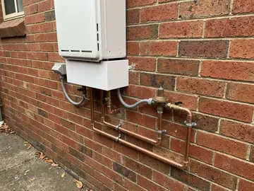 New continuous-flow gas hot water unit with copper pipework on a brick wall